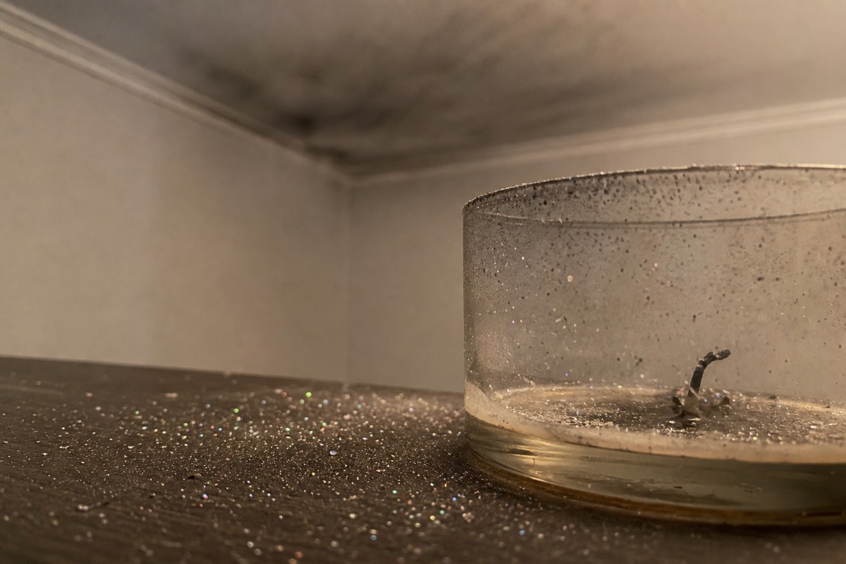 Minuscole paillette sparse sul tavolo intorno a una candela ormai consumata, sullo sfondo una sottile patina grigia di fuliggine sul soffitto.