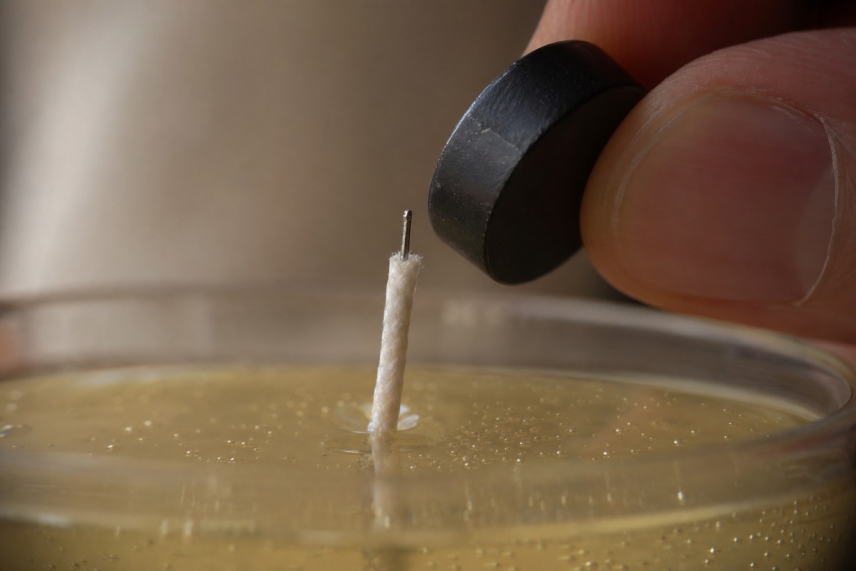 Dettaglio di uno stoppino estratto con sottile anima metallica e un piccolo magnete avvicinato al nucleo metallico dello stoppino