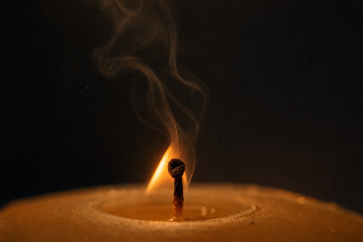 Stoppino di una candela con fiamma instabile e una scia di fumo nero che sale in una stanza buia