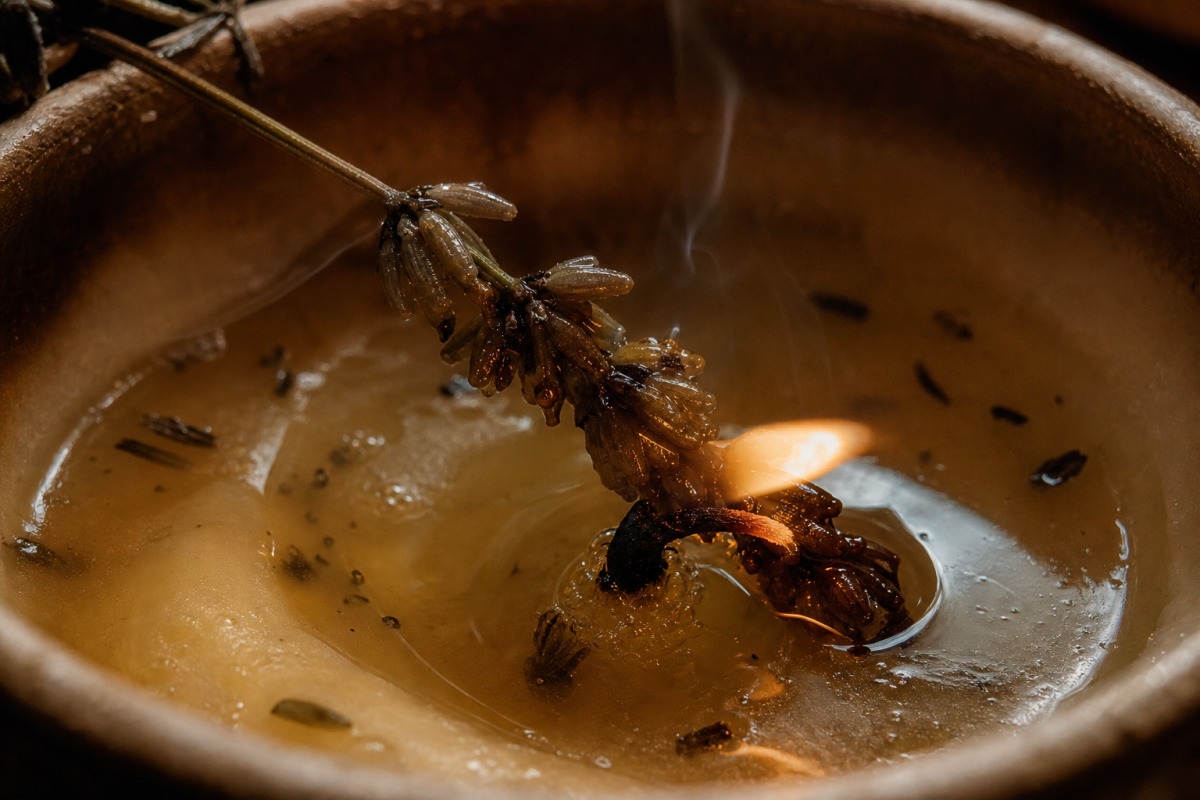 Una spiga di lavanda essiccata impregnata di cera si piega sullo stoppino in una pozza irregolare di cera fusa